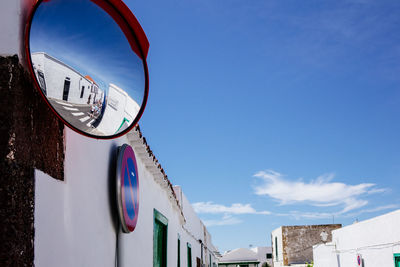 Road mirror by building against sky