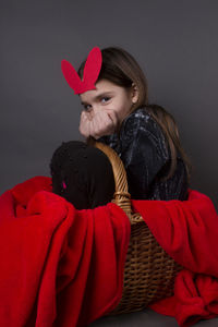 Portrait of smiling girl with costume rabbit ears sitting in basket against gray background