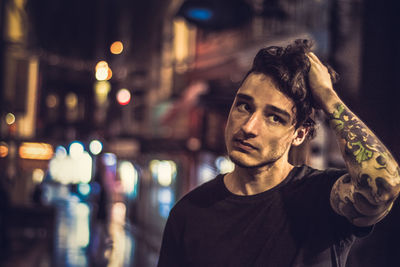 Thoughtful young man looking away while standing against buildings in city at night