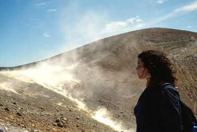 Side view of woman standing on mountain against sky