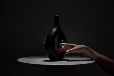 Cropped hand of woman by bottle and bubble against black background