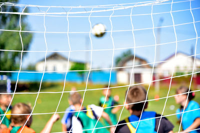 Children playing soccer on field seen through net