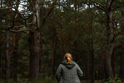 Back view of a young blonde woman hiking in forest. hiking woman walking in gloomy mystical forest