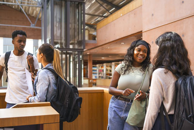 Multiracial male and female student friends talking while standing in university library