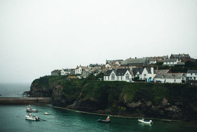 Boats in sea by buildings on cliff against clear sky in cornwall, united kingdom