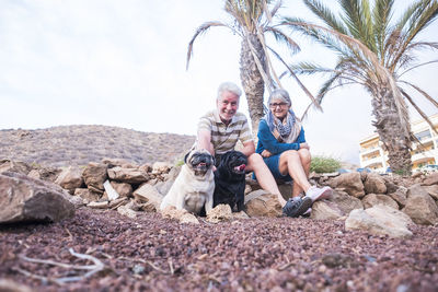 Senior couple sitting with dogs against sky