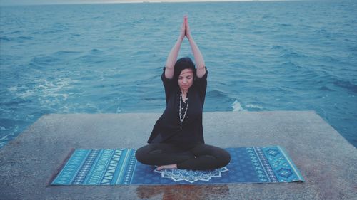 Full length of woman performing yoga against sea