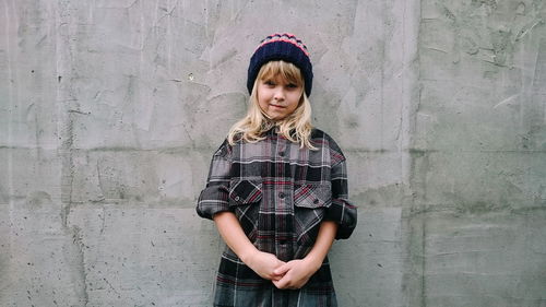 Portrait of blond girl standing against concrete wall
