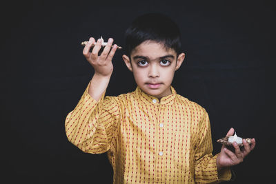 Portrait of boy holding candles standing against black background