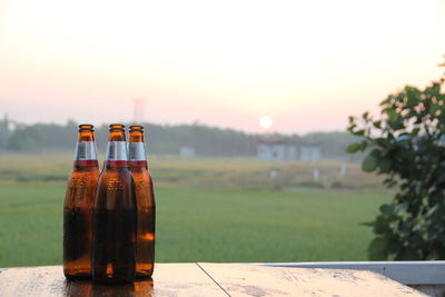 Glass of bottle on table against sky during sunset