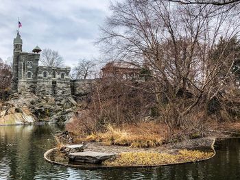 Bare tree by river against buildings