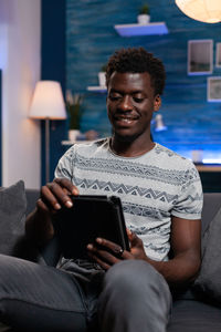 Smiling man using digital tablet sitting on sofa