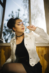 Young woman looking away while sitting on window