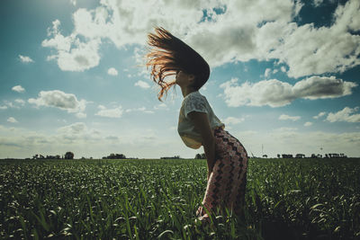 Side view of woman with long hair standing on field against sky