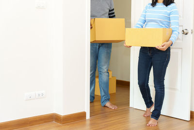 Low section of couple holding boxes while standing on hardwood floor at home