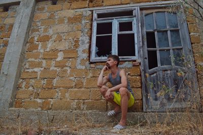 Full length of shirtless man sitting outside house