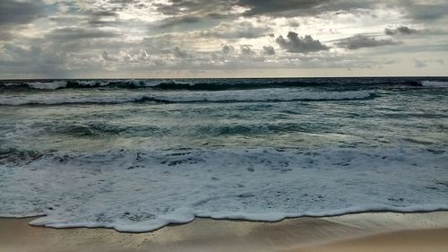 View of calm beach against cloudy sky