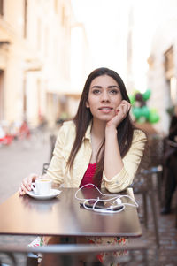 Thoughtful woman looking away while having coffee at sidewalk cafe