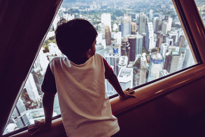 Rear view of boy looking through window