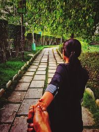 Woman holding cropped hand while standing on footpath in park