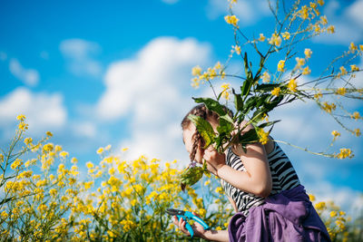 Cute girl holding flower while standing against sky