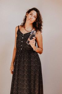 Portrait of young woman holding water bottle while standing against wall