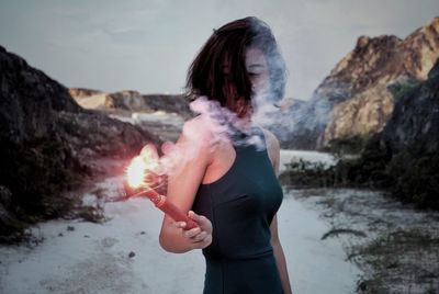 Young woman smoking while standing on mountain against sky