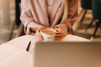 Human hands are typing on a laptop standing on a wooden table. desktop with a coffee. top view