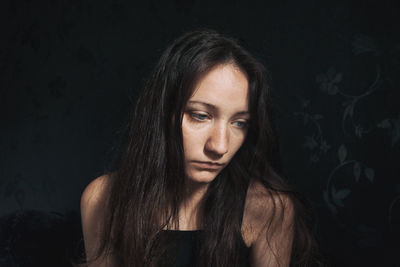 Sad young woman against black background