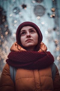 Thoughtful young woman wearing warm clothing while looking away against lights