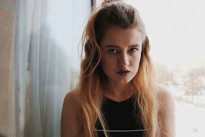 Portrait of beautiful woman against window at home