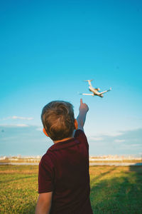 Rear view of man flying bird on field against sky