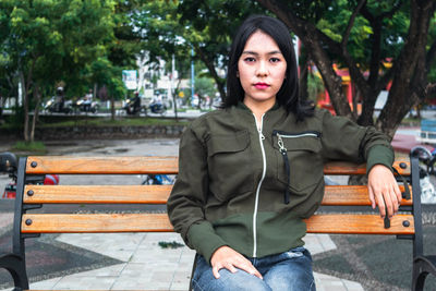 Portrait of young woman sitting on bench in park