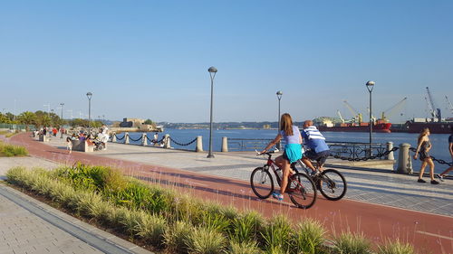 People cycling on promenade against clear sky