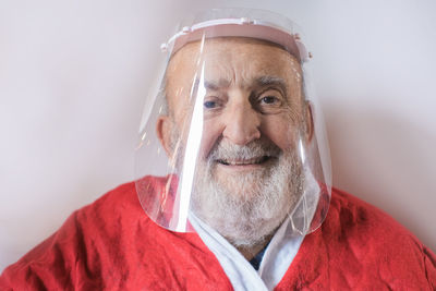 Close-up portrait of senior man wearing face shield against white background