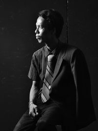 Young man looking away while sitting against wall