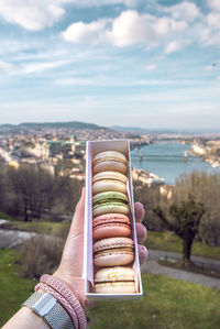 Close-up of hand holding macaroons in box against sky