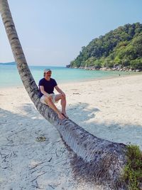 Rear view of man sitting on palm palm trunk on beach