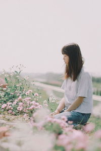 Woman sitting by flowering plants against sky