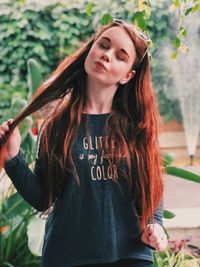 Young woman with eyes closed holding her hair while standing against plants