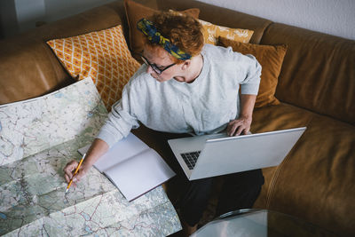 Side view of elderly woman planning trip on map and using laptop at home