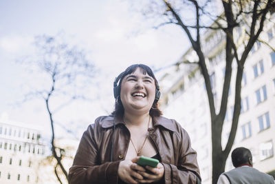 Young woman laughing while listening music through wireless headphones