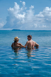 Rear view of woman and man swimming in infinity pool against sea