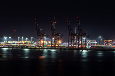 Illuminated pier by harbor against sky at night