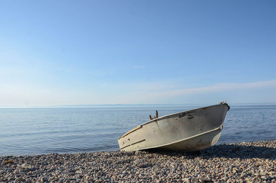 Scenic view of rowboat on rocky beach against sea and sky