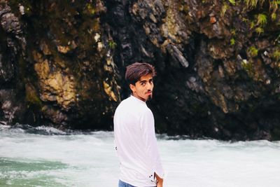 Portrait of young man standing against riverbank