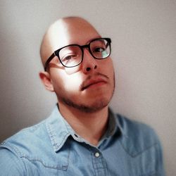 Close-up portrait of man wearing eyeglasses against wall