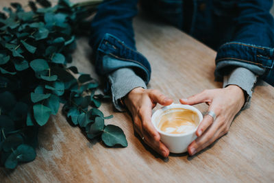 Cropped hands of woman holding coffee cup on table