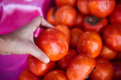 Close-up view of hand holding ripe sweet persimmon fruit at market