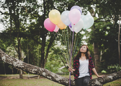 Full length of woman with pink balloons standing against trees